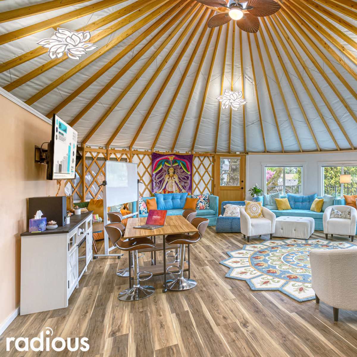 A spacious round room with a wooden ceiling and large windows, furnished with various seating options and a central table.