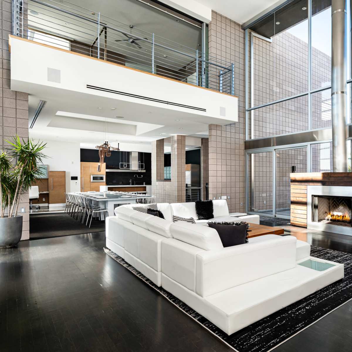 A modern living space featuring a white sectional sofa, a fireplace, large windows, and an open layout with a dining area in the background.