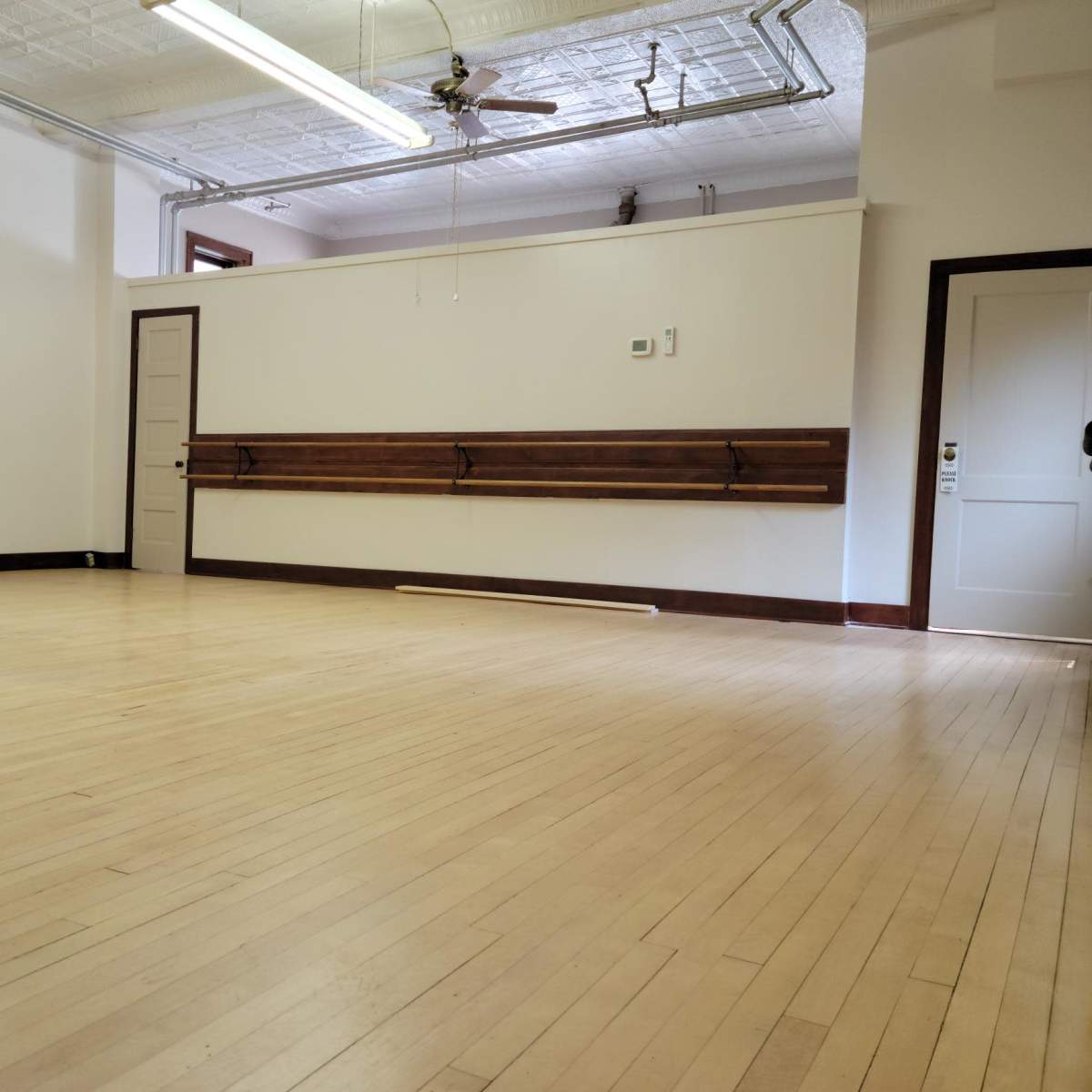 An empty room with wooden floors, a white wall, and a door on one side.