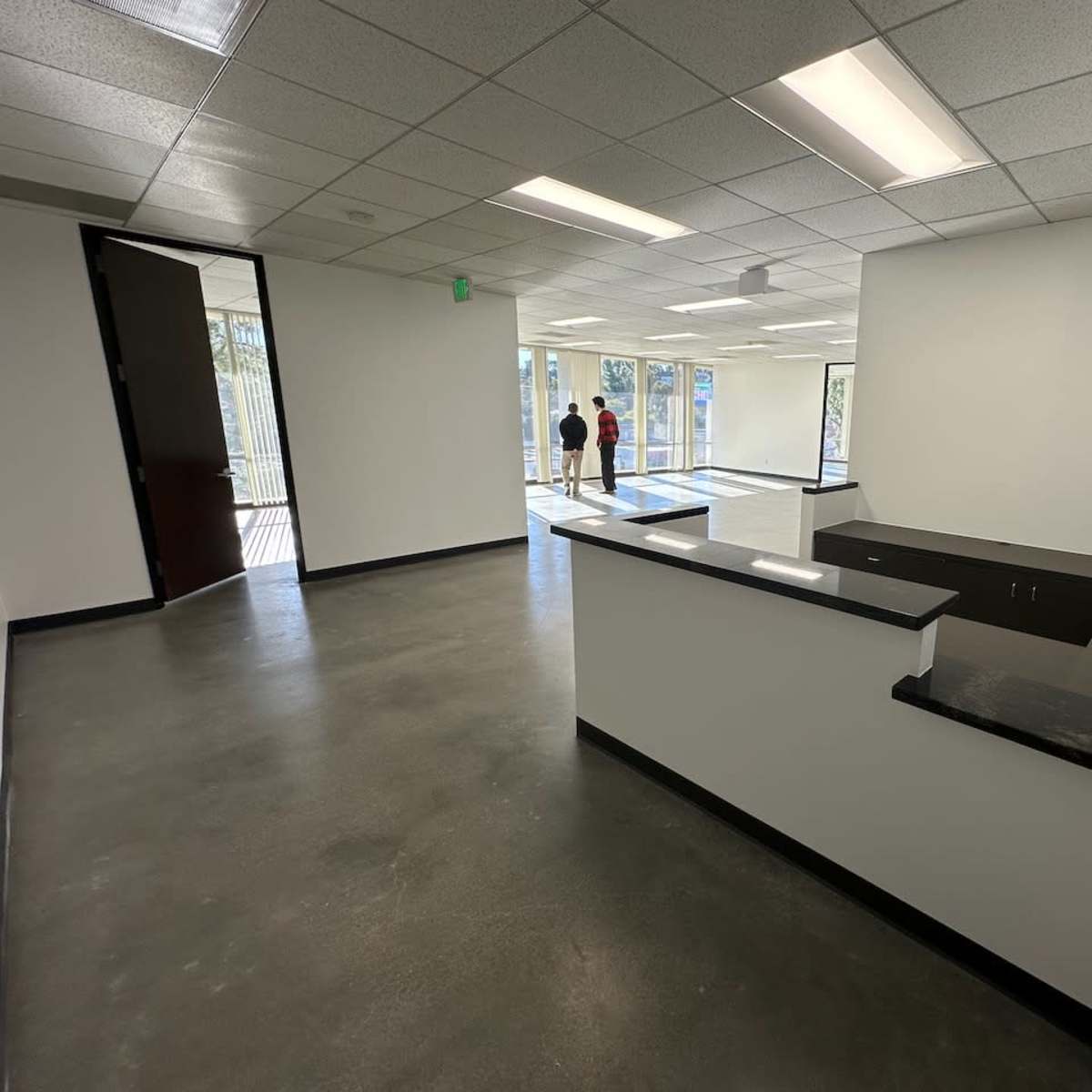 A partially empty office space with a reception desk on one side and large windows letting in natural light on the opposite side.