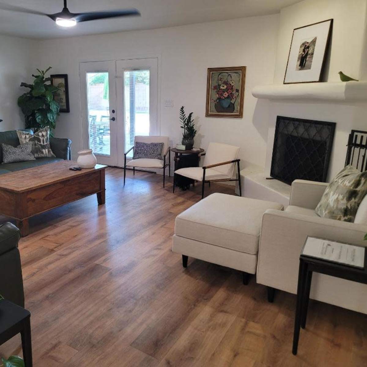 The living room features a green leather sofa, a wooden coffee table, a light-colored armchair, and large windows that open to a patio.