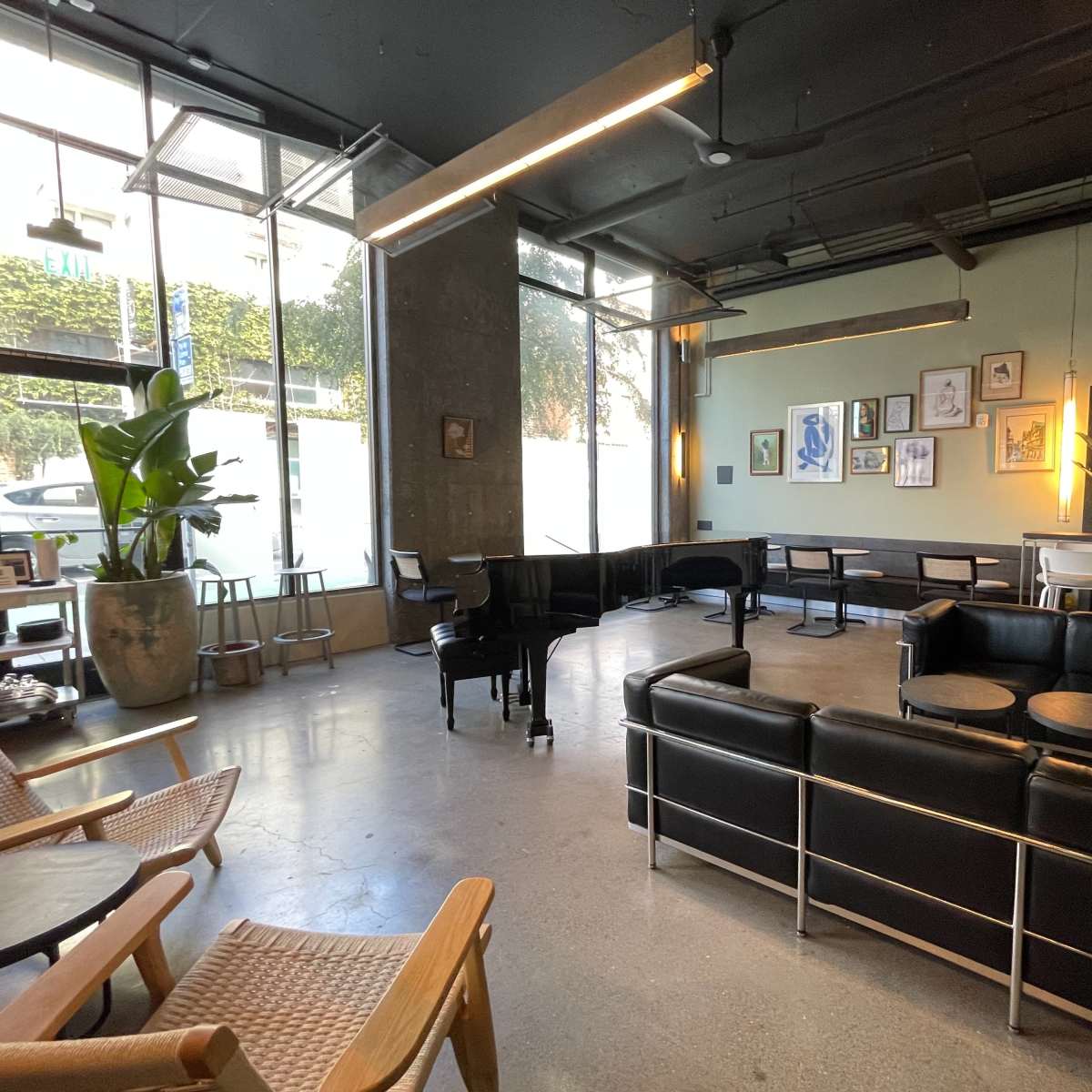 A modern café features black leather seating, wooden chairs, and large windows allowing natural light to enter.