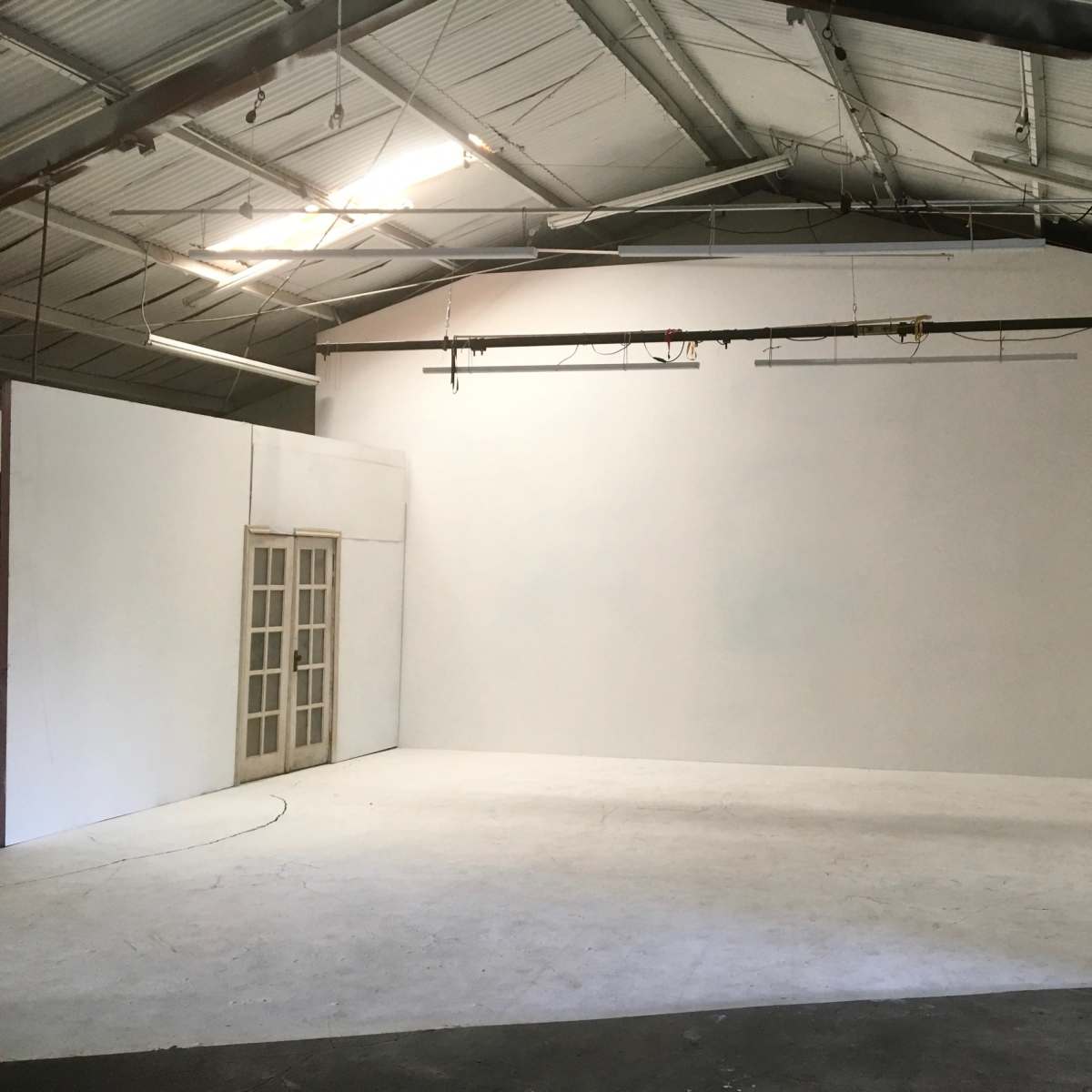A large, empty studio space with white walls and a set of French doors on one side.