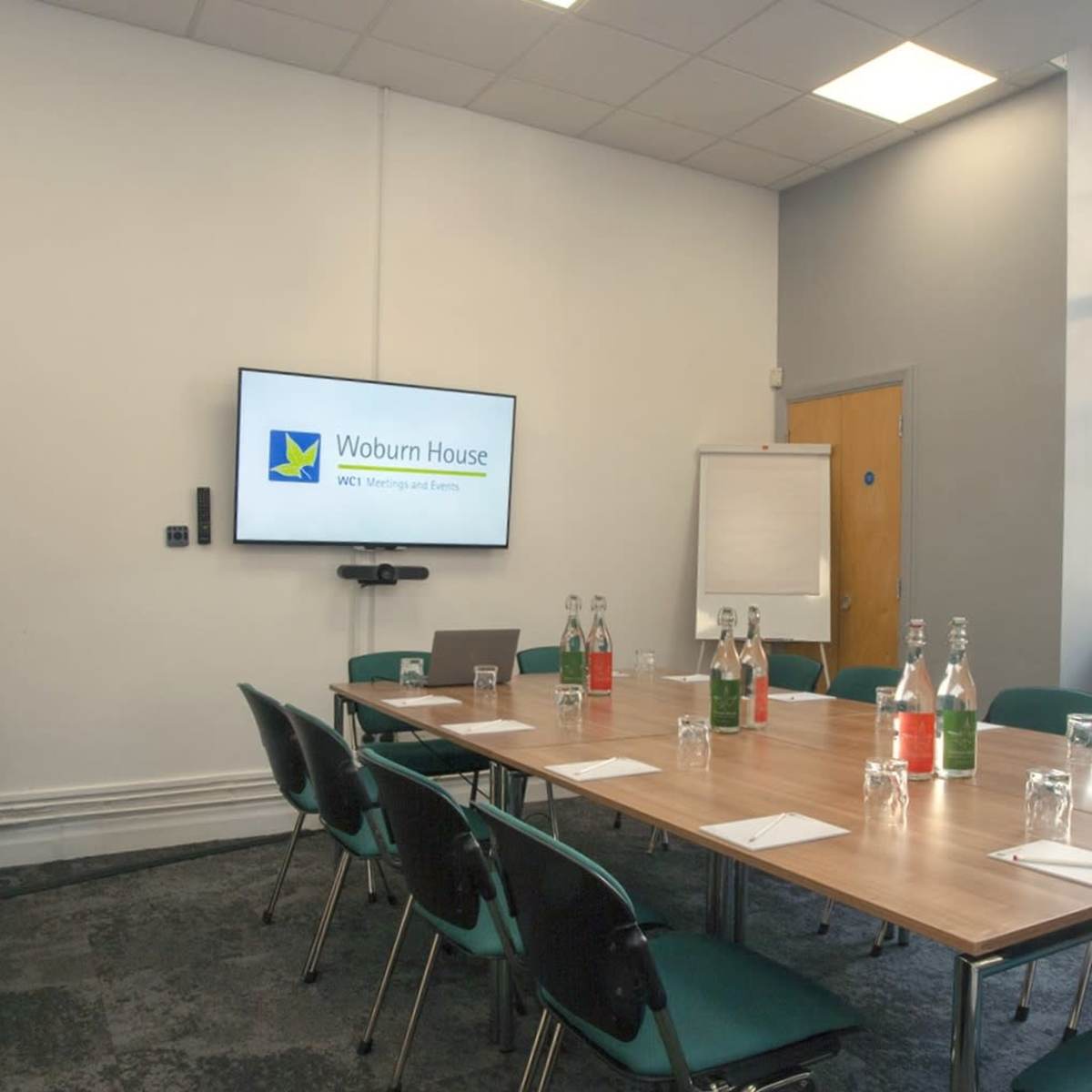 A meeting room is set up with a large table, chairs, a presentation screen, and water bottles.