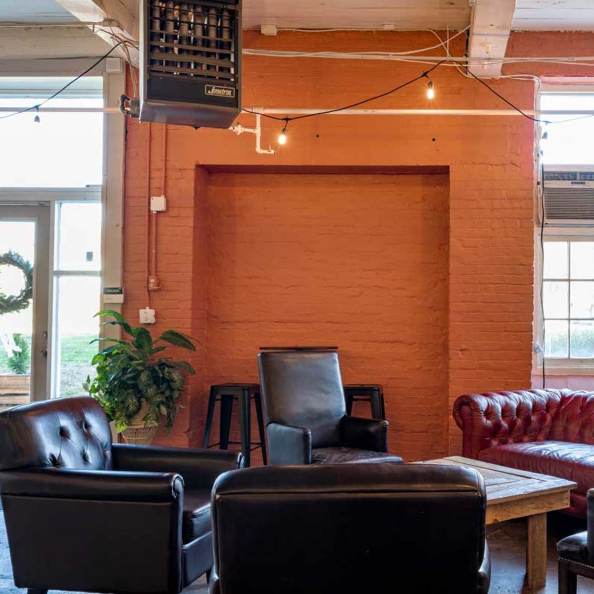 A cozy lounge area features a red leather sofa, several black chairs, and a small wooden table, with a Christmas tree in the corner and string lights overhead.
