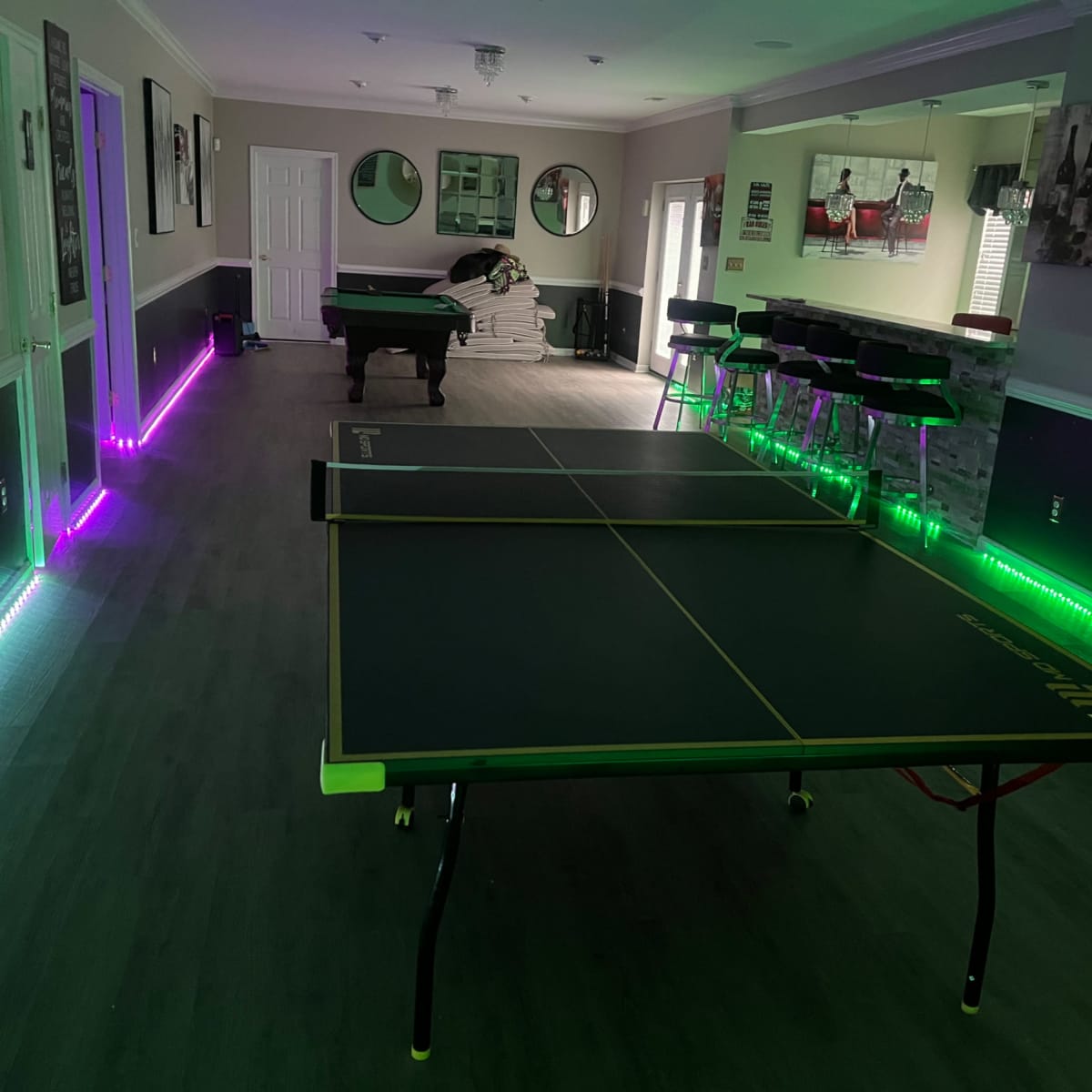 A recreation room with two ping pong tables and LED strip lighting along the floor, creating a vibrant atmosphere.