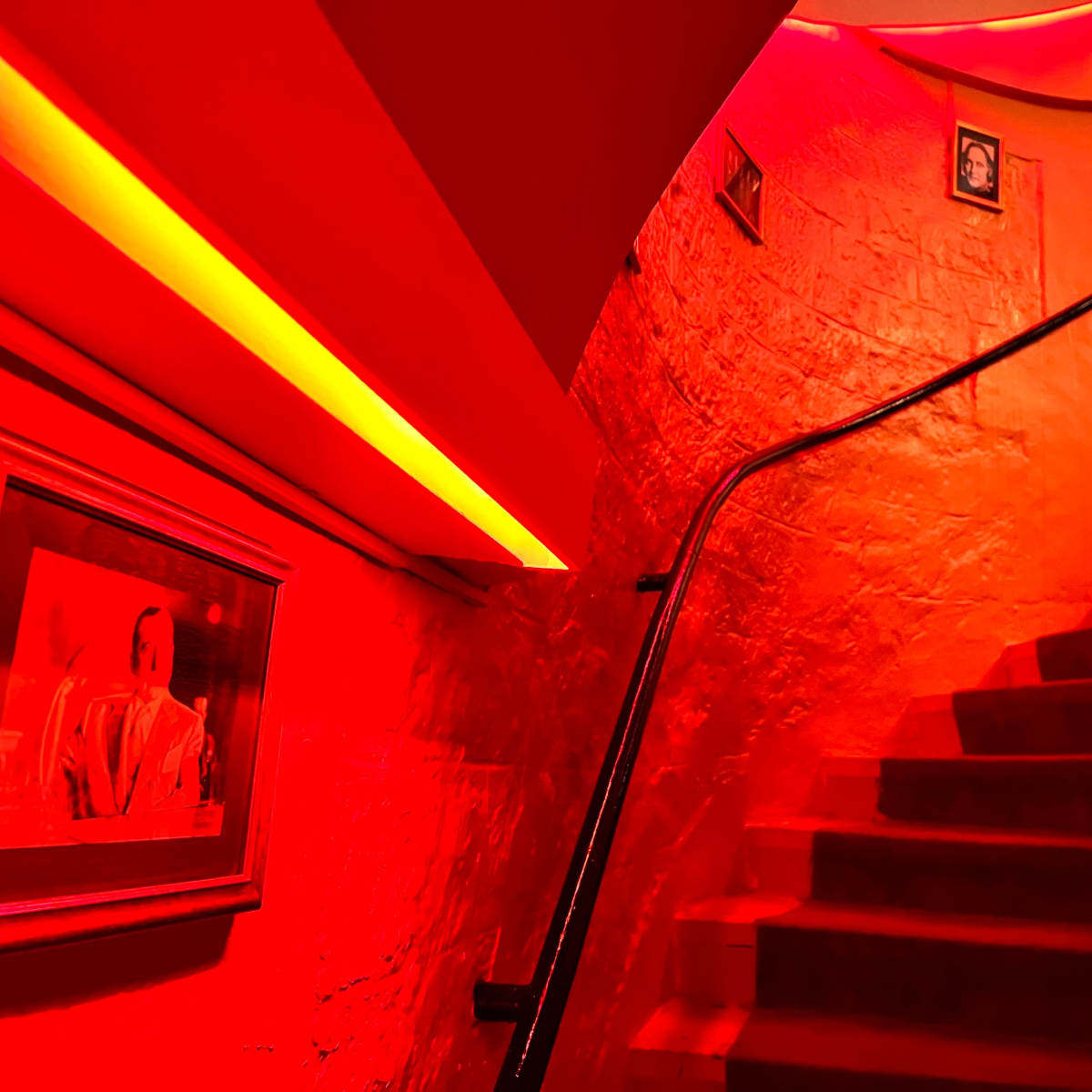 A staircase illuminated by red lighting leads upwards, with framed pictures along the walls.