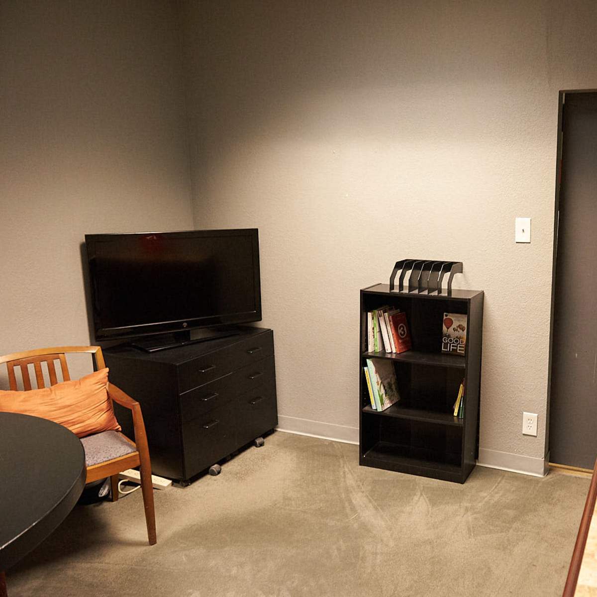 A small meeting room featuring a television, a black bookshelf with books, and an orange decorative vase on a table.