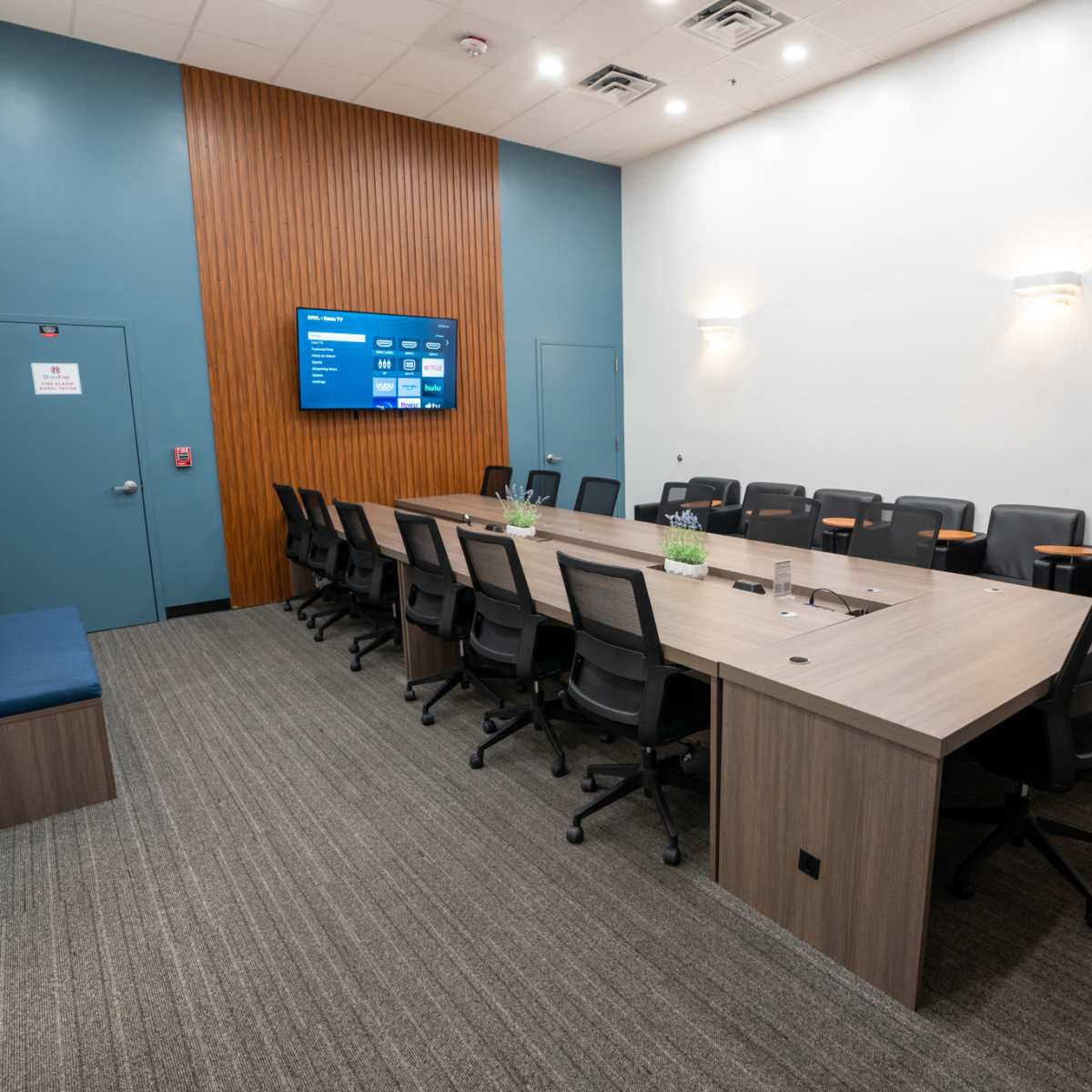 A modern conference room equipped with a long table, multiple chairs, and a large screen on the wall.