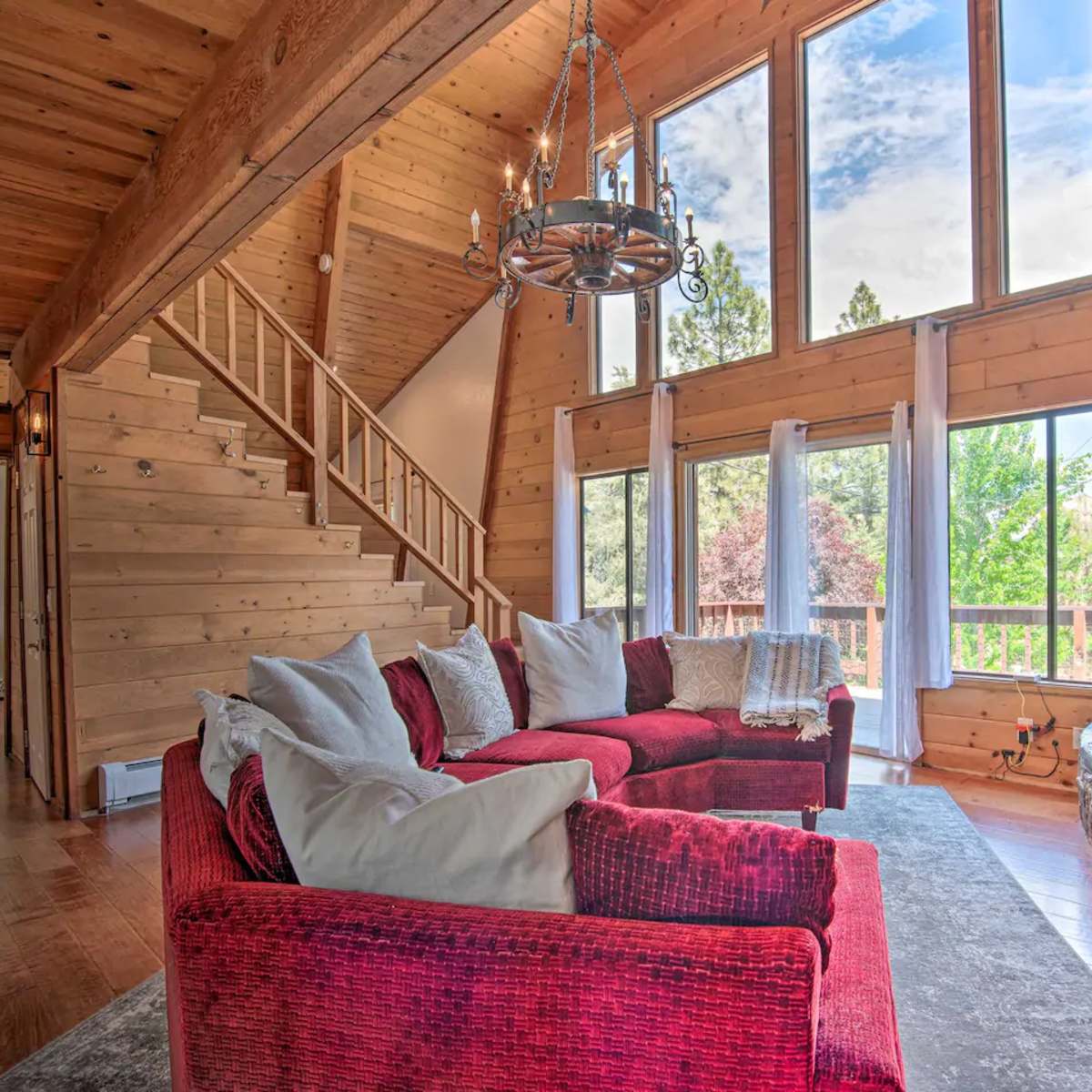 A cozy living room with a red sectional sofa, a stone fireplace, and large windows letting in natural light.