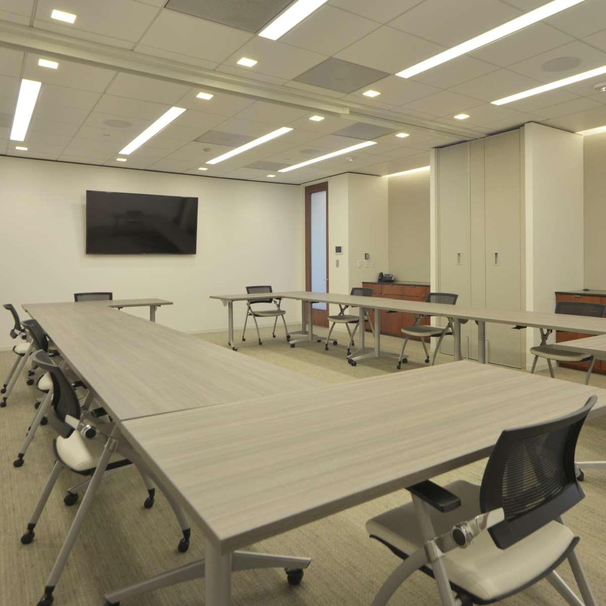 A modern conference room features multiple tables arranged for meetings, with chairs and a wall-mounted screen.