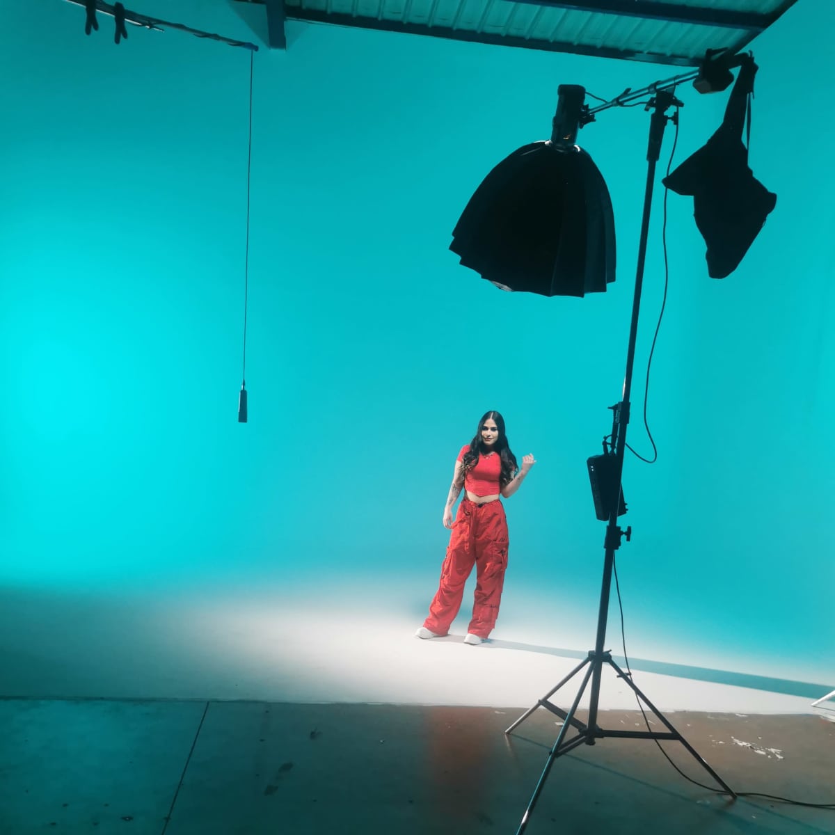 A person poses in a studio with a turquoise backdrop and focused lighting.