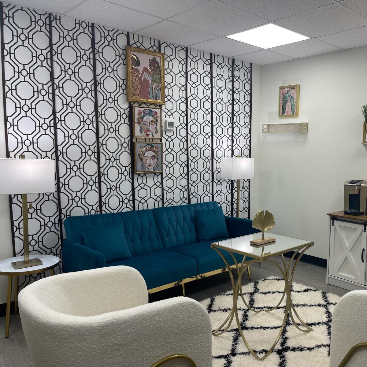 A modern lounge area featuring a teal sofa, two white armchairs, a coffee table, and decorative artwork on the walls.