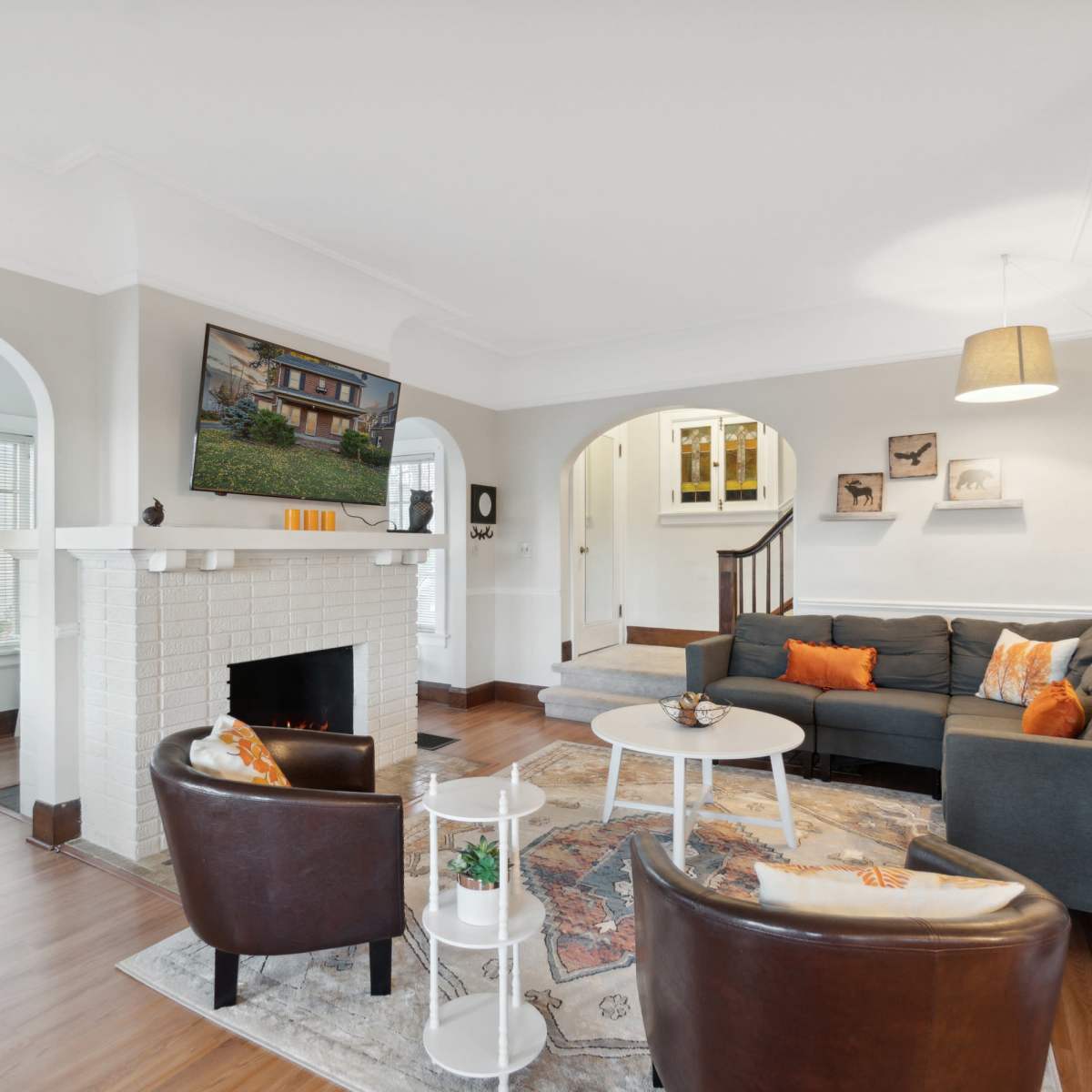 A living room featuring a fireplace with a television mounted above it, two armchairs, a coffee table, and an open layout connecting to adjacent spaces.