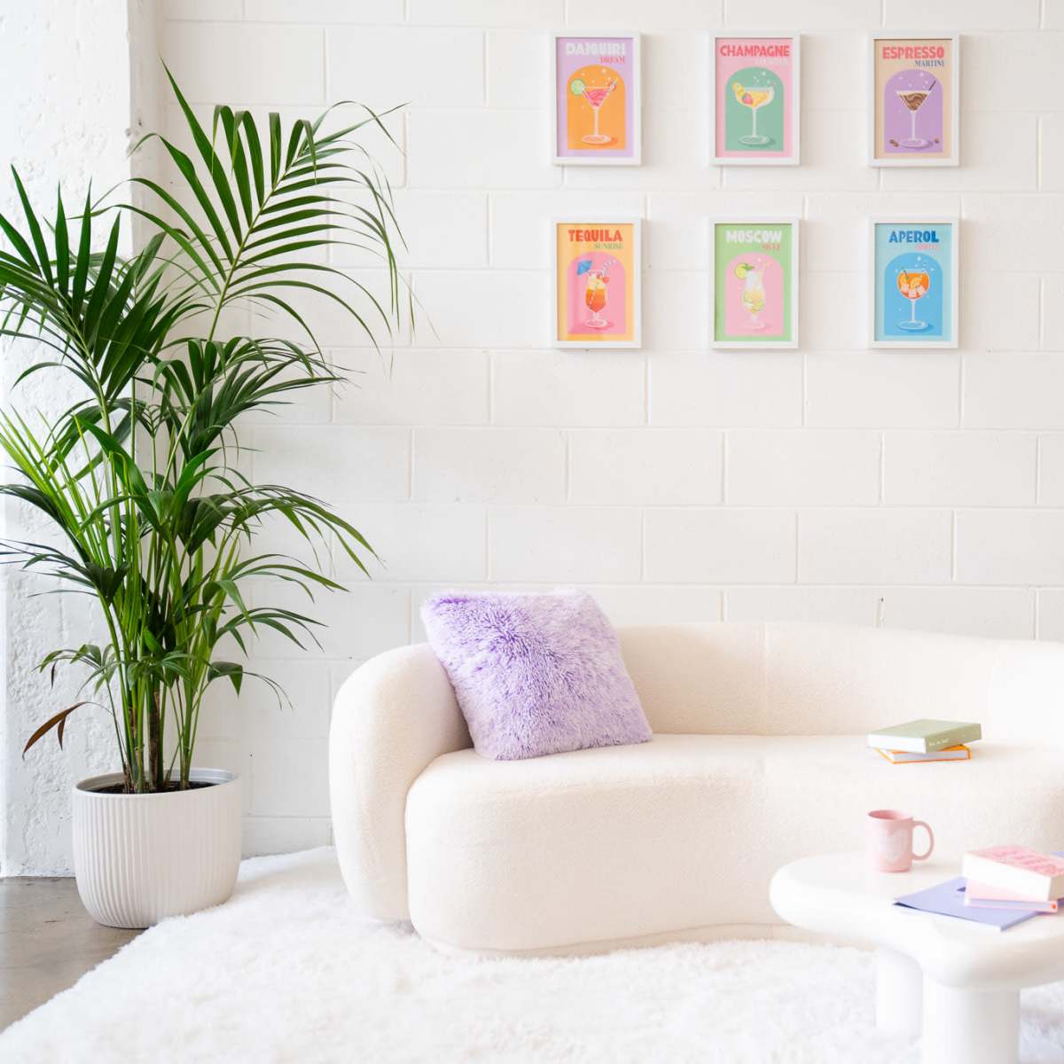 A modern seating area features a white sculptural couch, a round coffee table, and a side table with a pink telephone, accompanied by potted plants and colorful art prints on the wall.