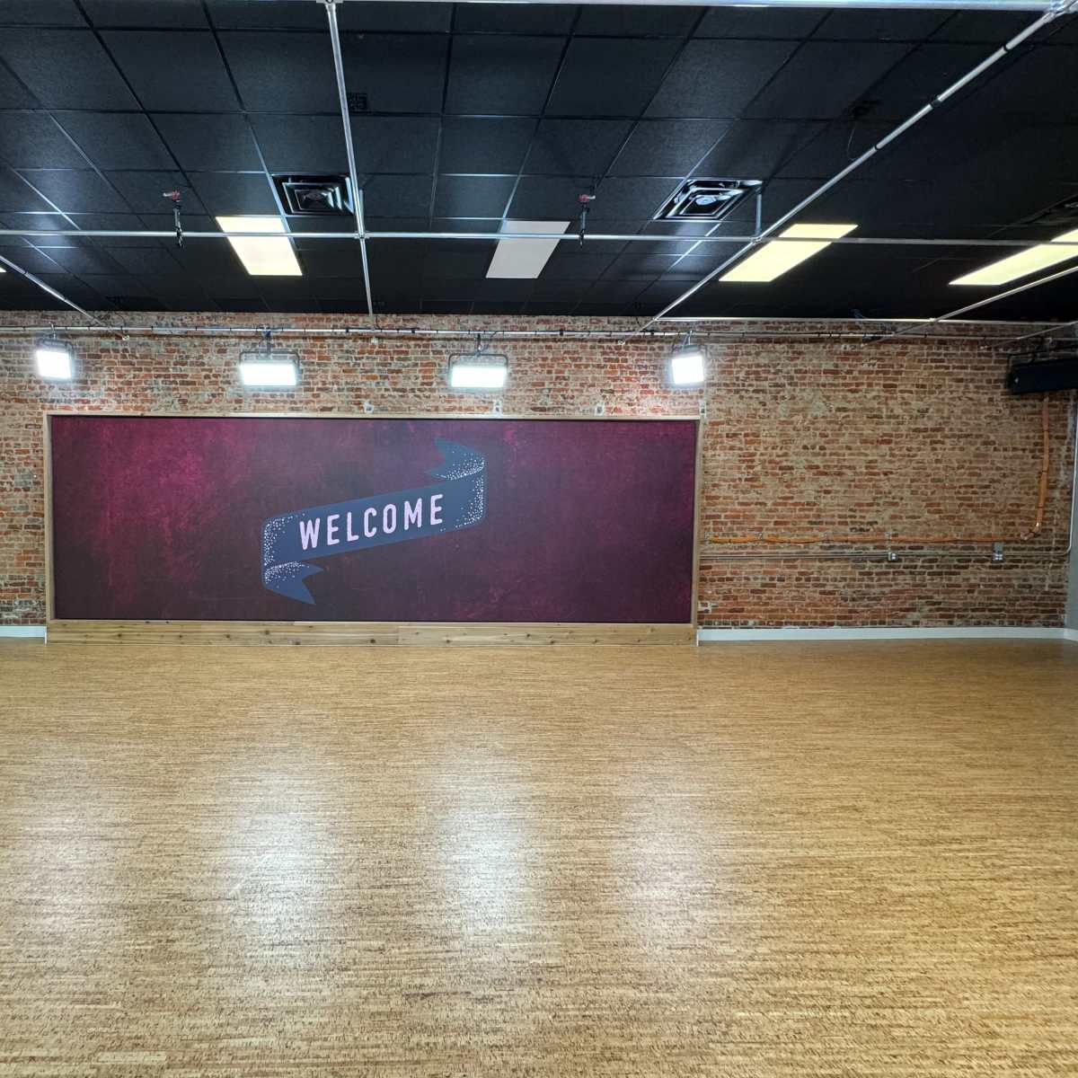 A spacious room with a wooden floor and a red brick wall featuring a "WELCOME" sign.