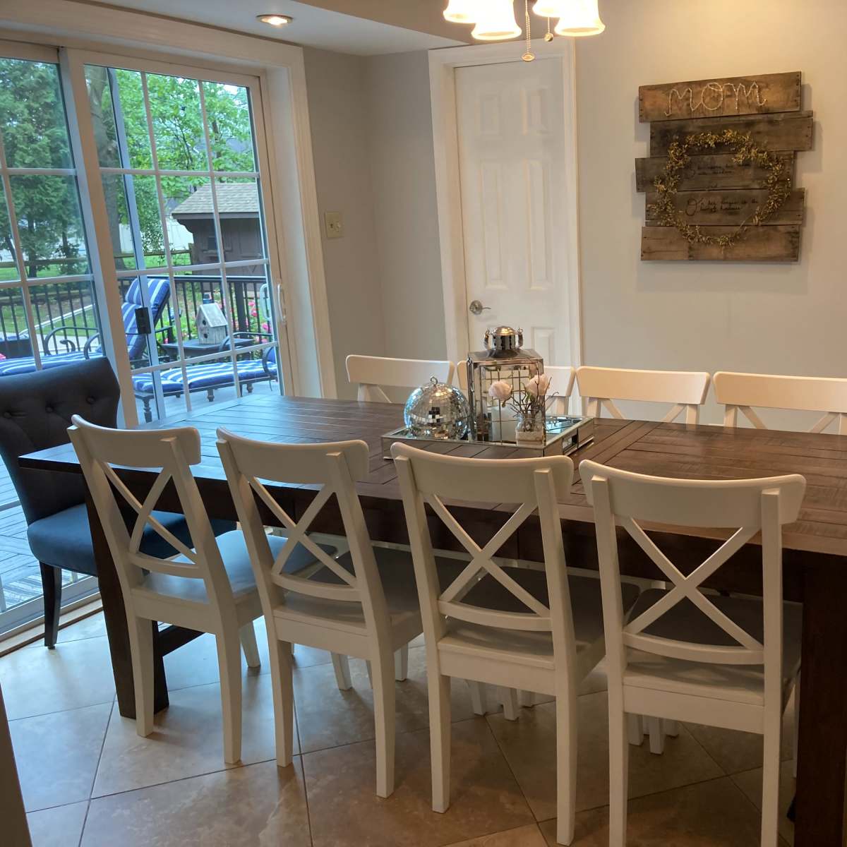 A dining area with a long wooden table surrounded by white chairs, set near a large window that provides a view of the outdoors.