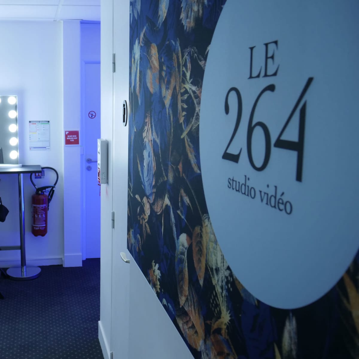 A bright, modern video studio with two illuminated mirrors and high stools against a wall featuring the text "LE 264 studio vidéo."