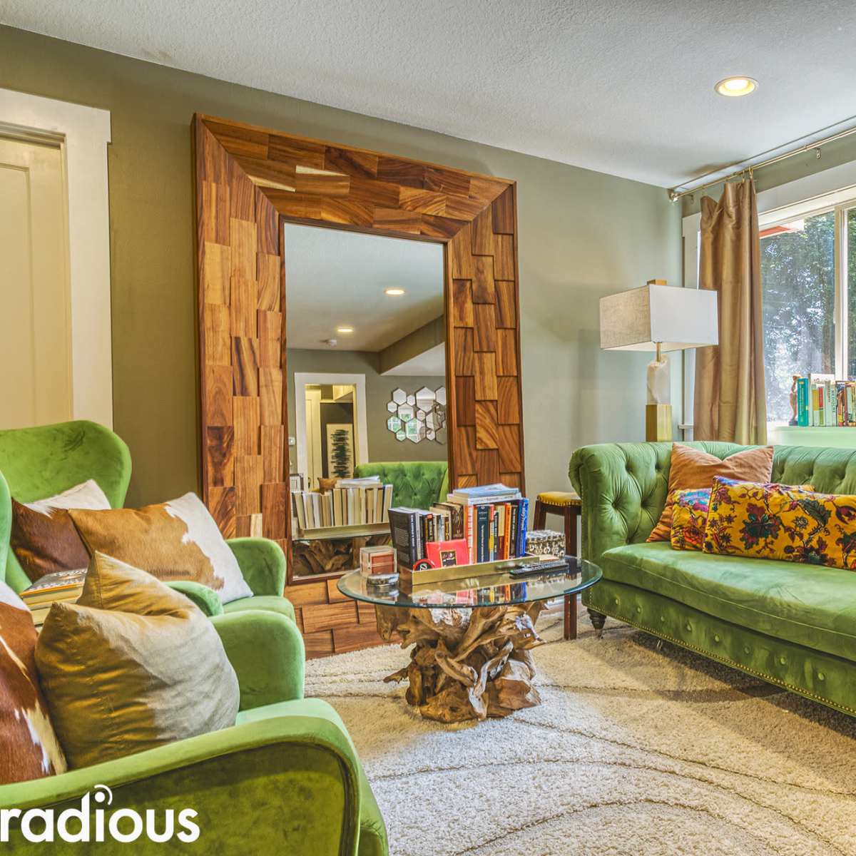 A cozy living room features a green velvet sofa, a round glass coffee table, and a large rectangular mirror framed with wood.