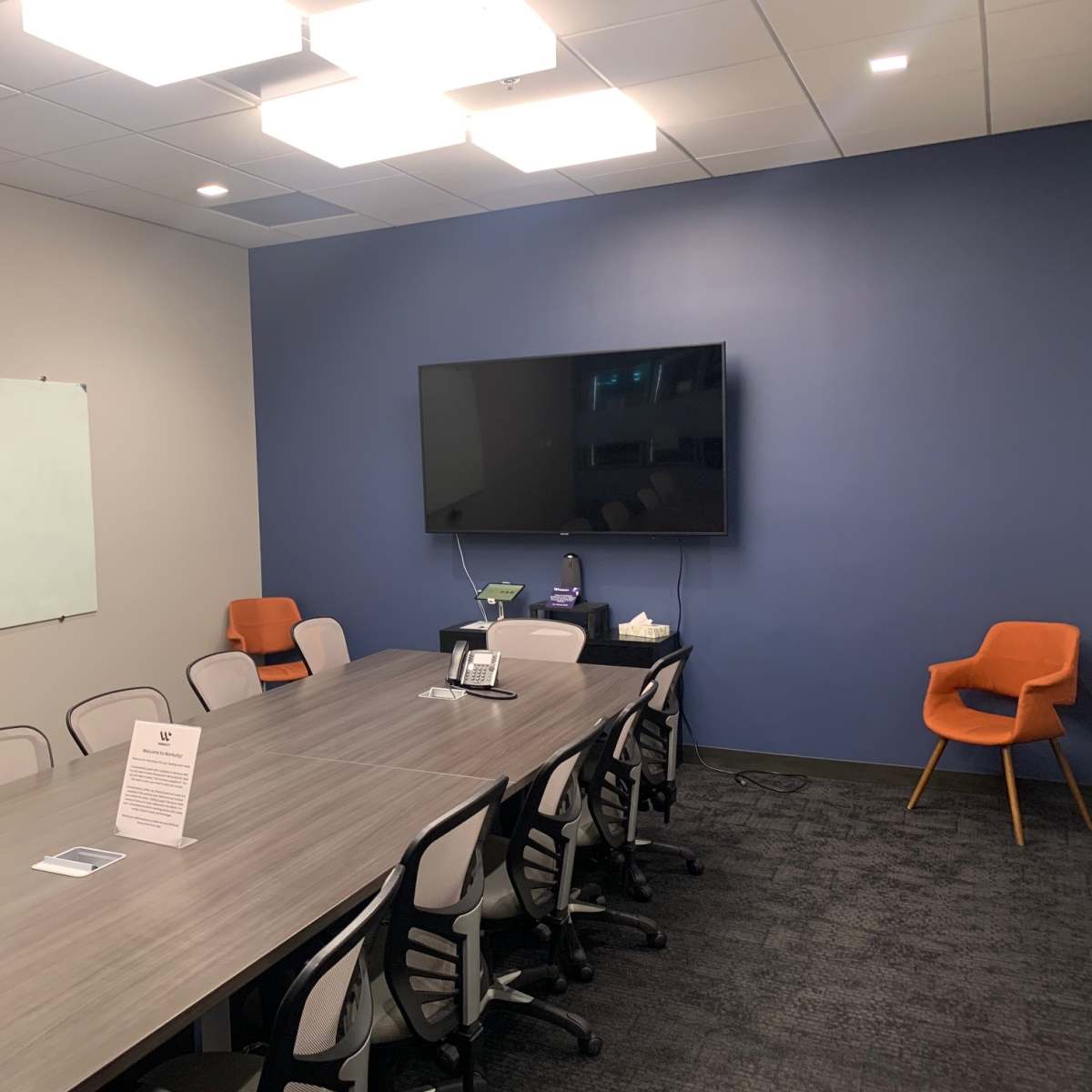 A modern conference room with a large table, chairs, a whiteboard, and a wall-mounted television.