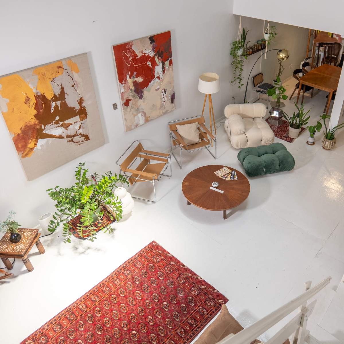 A bright, airy living space with a mix of modern furniture, plants, and artworks arranged around a circular coffee table on a white floor.