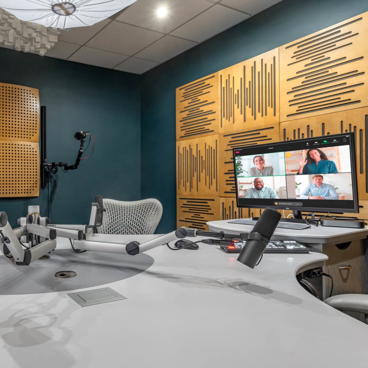 A modern recording studio equipped with microphones, a control panel, and a screen displaying video participants on a wooden wall background.