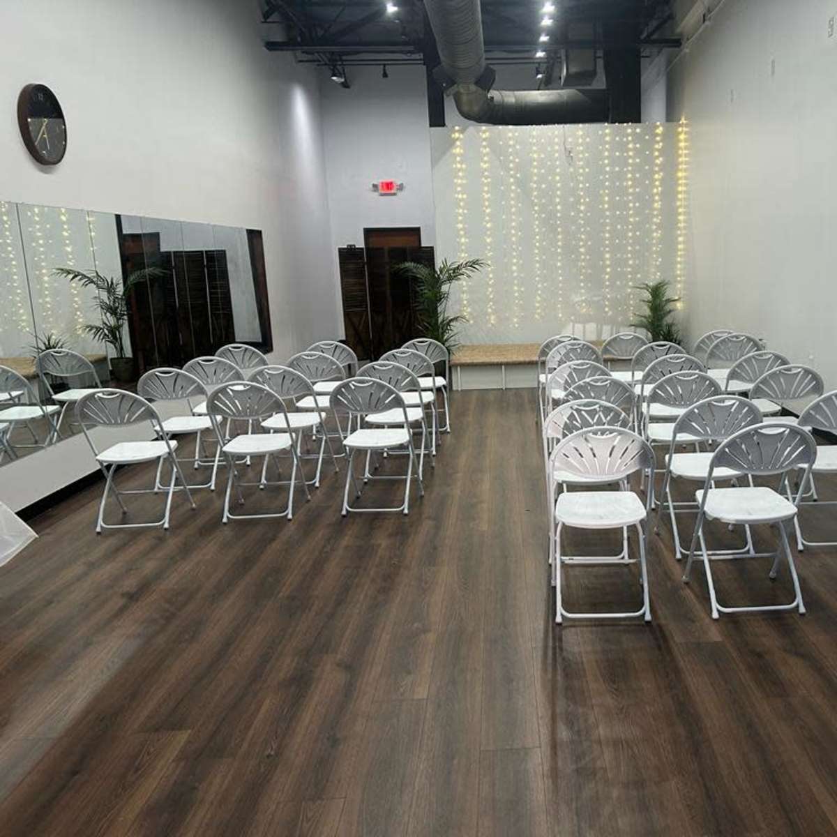A spacious room arranged with white folding chairs facing a decorated backdrop of string lights.