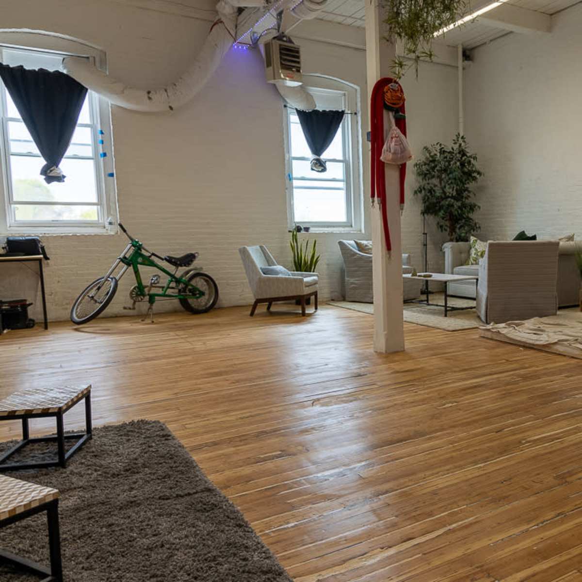A spacious, well-lit room with wooden floors featuring a large red heart decoration on the wall, seating areas with chairs and a sofa, and a bicycle leaning against the wall.