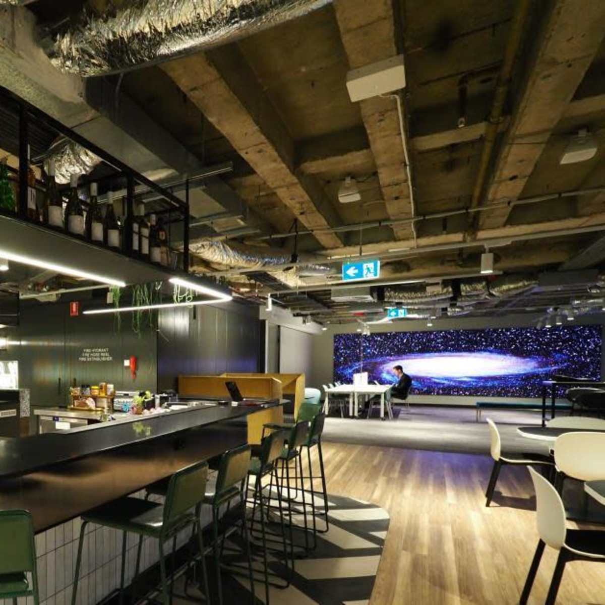 A modern office space featuring a central bar with green stools, a preparation area, and a wall decorated with a starry night mural.