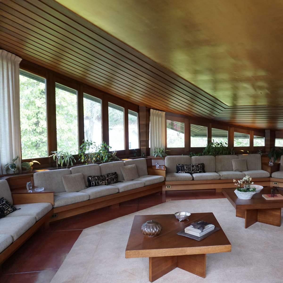 A spacious living room with a large, curved sofa, wooden furniture, and large windows allowing natural light to enter.