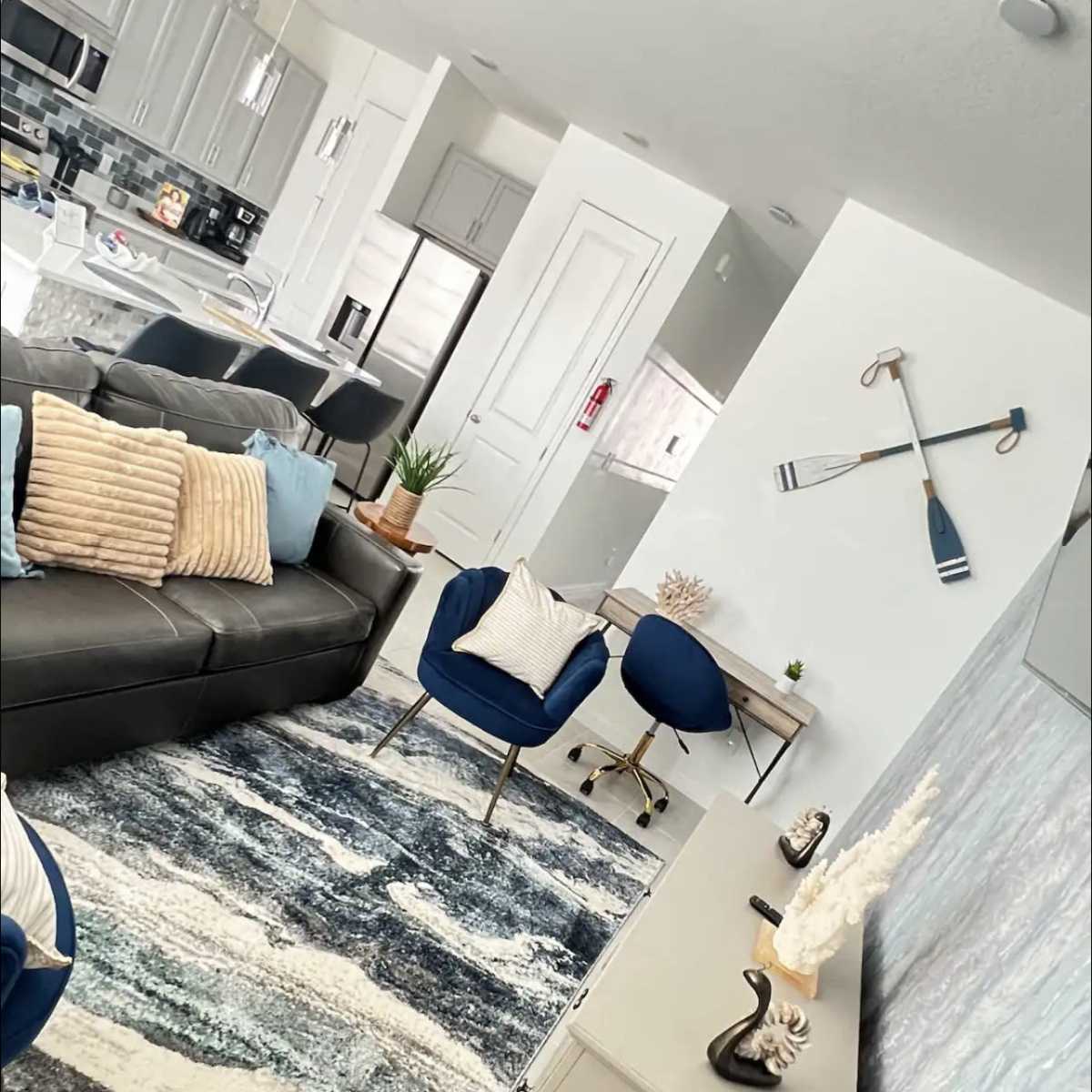 A modern living room with a gray sofa, blue accent chairs, and a decorative wall featuring oars, along with a light-colored area rug.