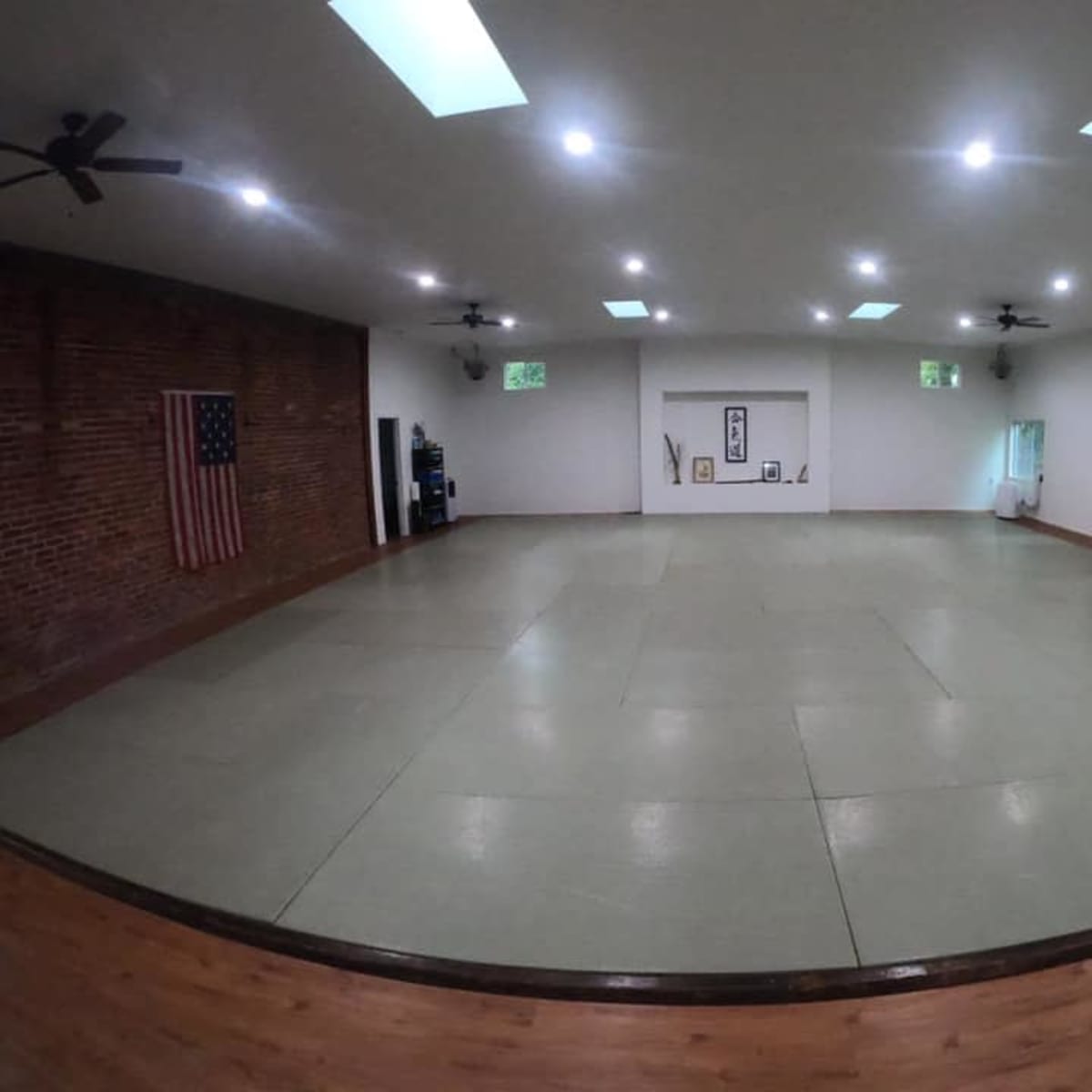 A large, empty martial arts studio with a wooden floor and padded mats, featuring an American flag on one wall.