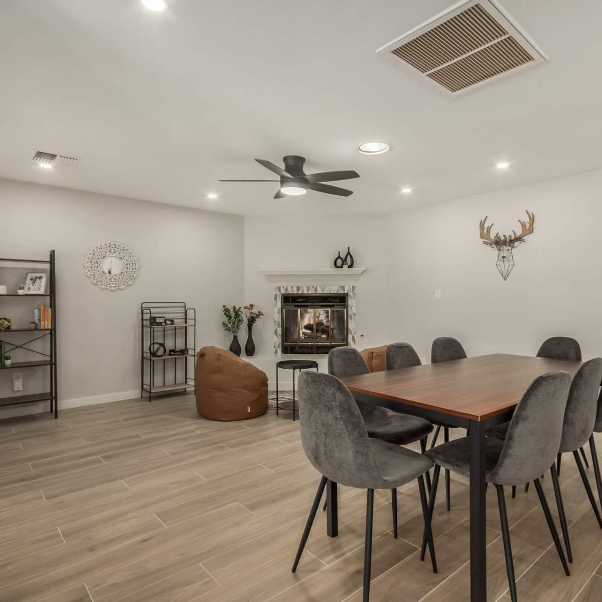 A modern living space features a dining table with six chairs, a fireplace, and various decorative elements against light-colored walls.