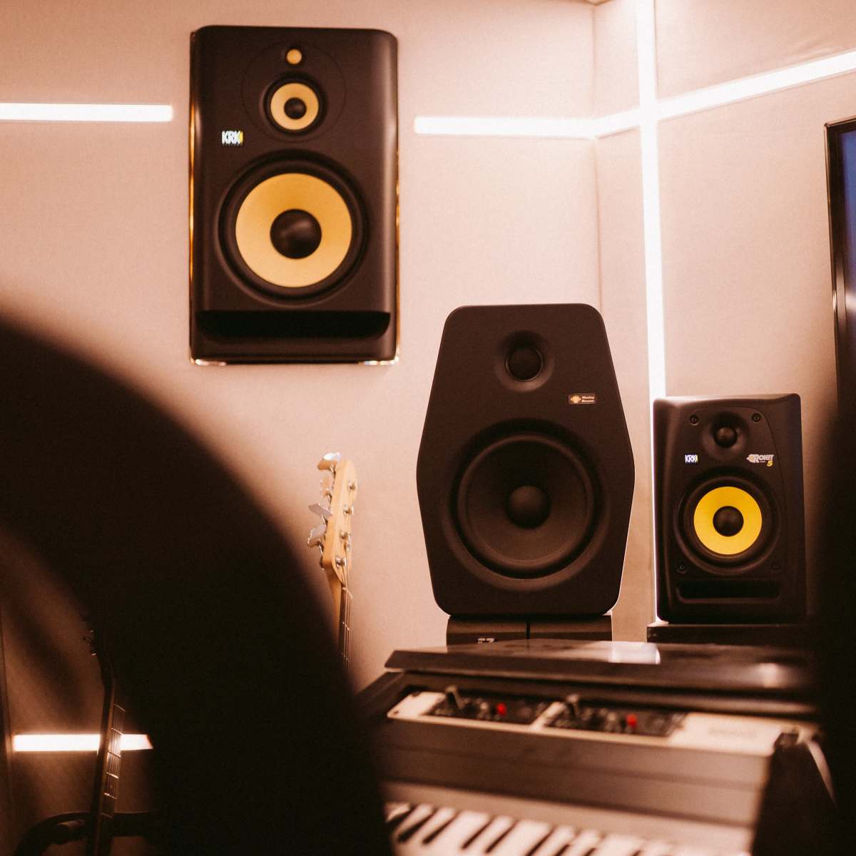 A music studio environment featuring wall-mounted speakers and a keyboard in the foreground.