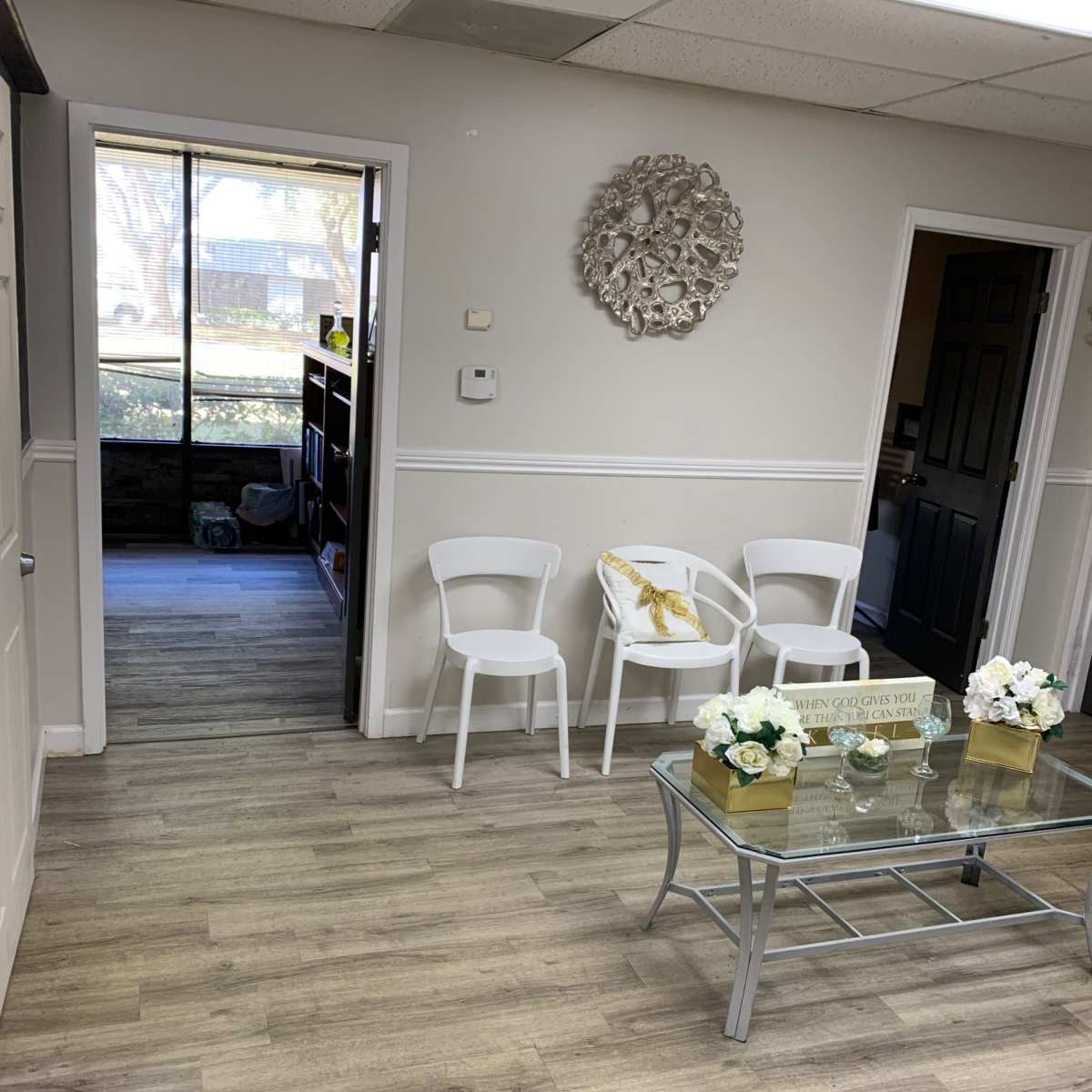 A waiting area with white chairs, a glass coffee table with decorative items, and a doorway leading to another room.