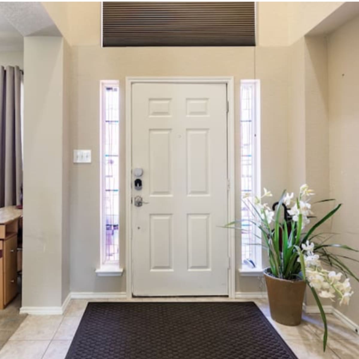A home's entrance with a white front door, beige walls, a tiled floor, and a potted plant beside the door.