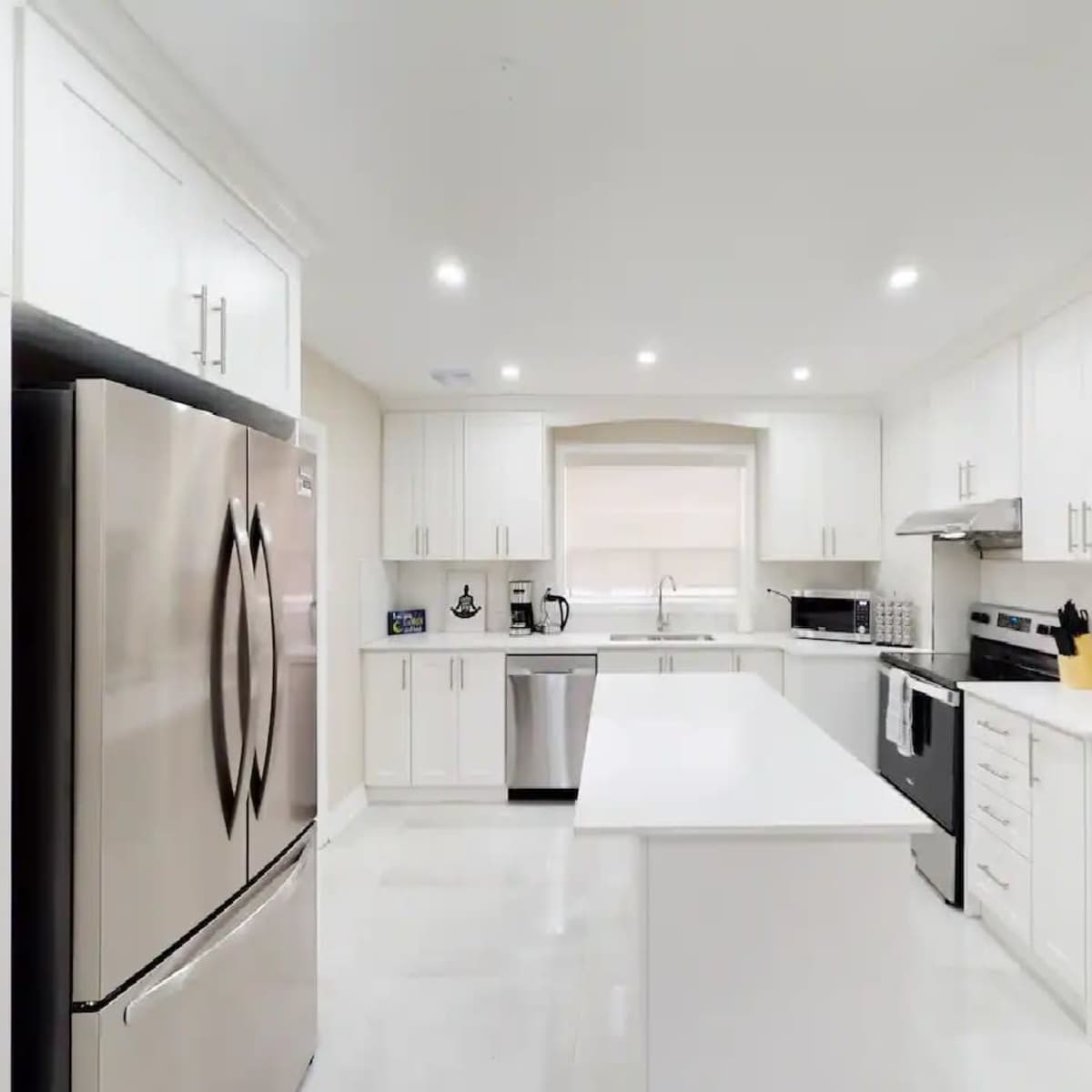 A modern kitchen featuring white cabinetry, stainless steel appliances, and a large island with a countertop.