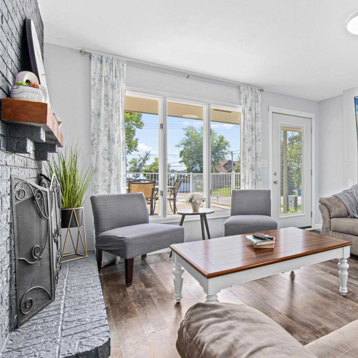 A cozy living room features a large sectional sofa, two armchairs, a wooden coffee table, and a mounted television, with large windows letting in natural light.