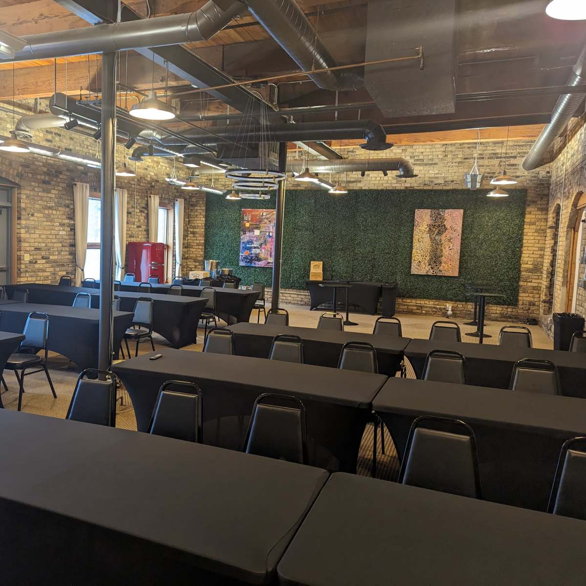 A large meeting room with several rows of tables covered in black tablecloths and a green wall featuring artwork in the background.