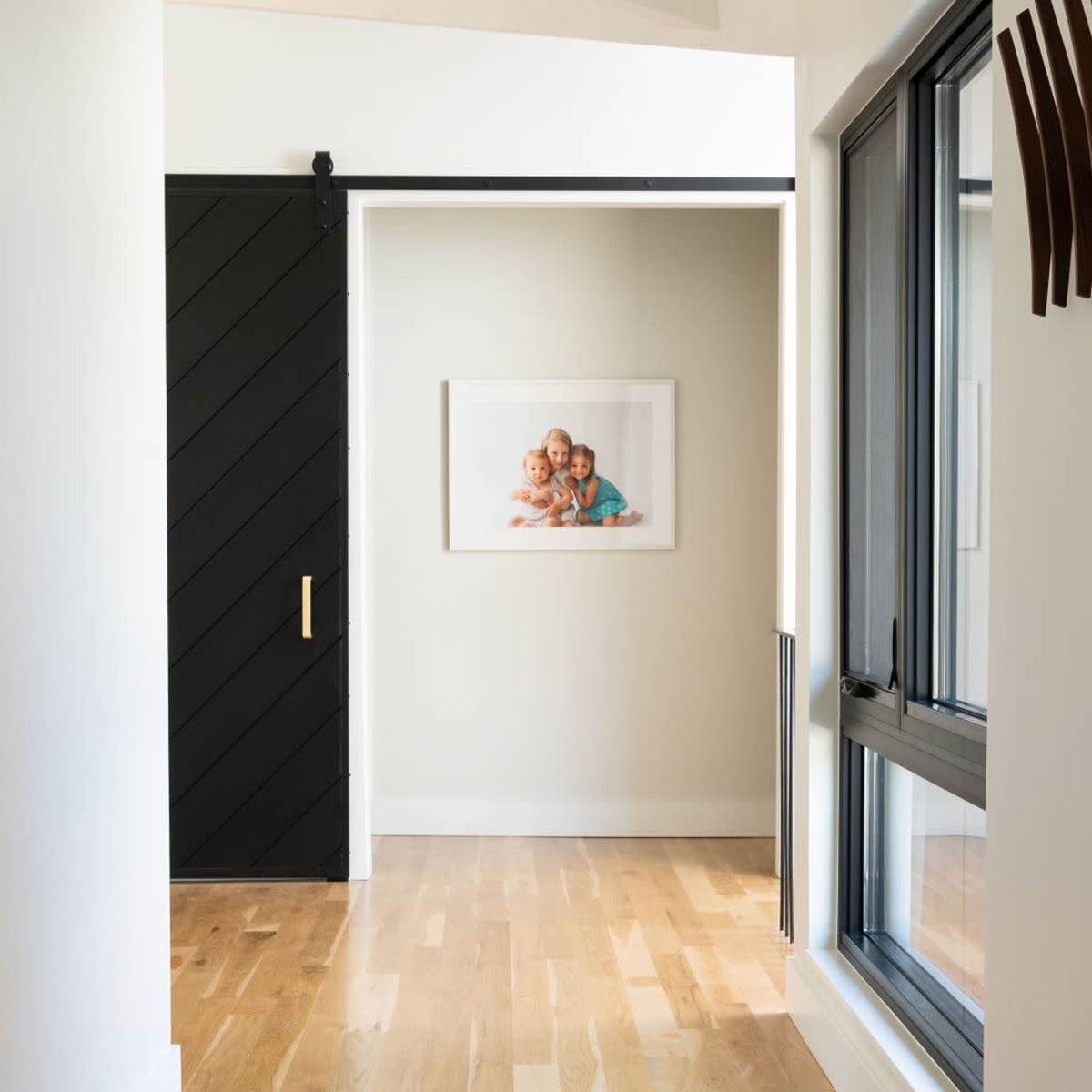 A narrow hallway features wooden flooring, a sliding black door, and a framed picture of children on the wall.