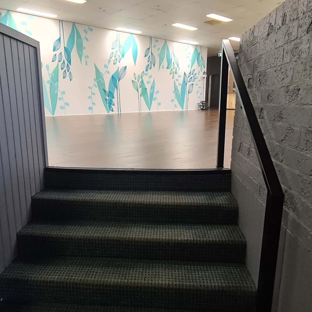 A stairway leading up from a narrow hallway to a well-lit room with a patterned wall.