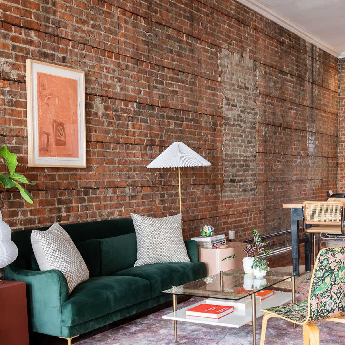A modern living room with a green sofa, a glass coffee table, a decorative lamp, and a brick wall backdrop.