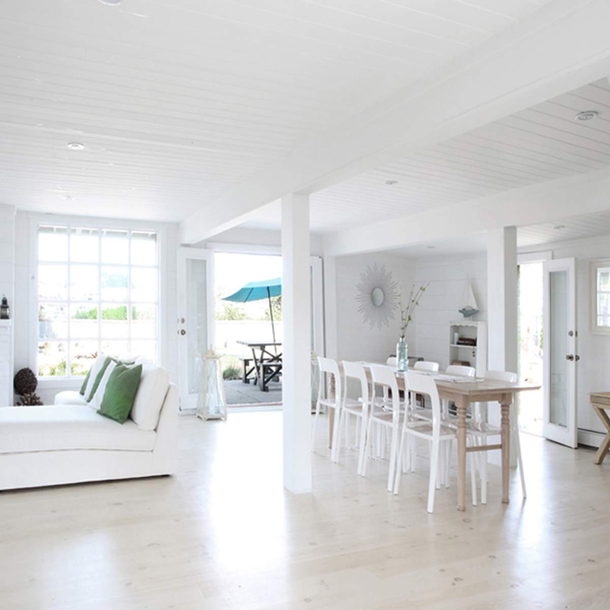 A bright, open-concept interior of a house with white walls, a fireplace, dining area, and a staircase leading to an upper level.
