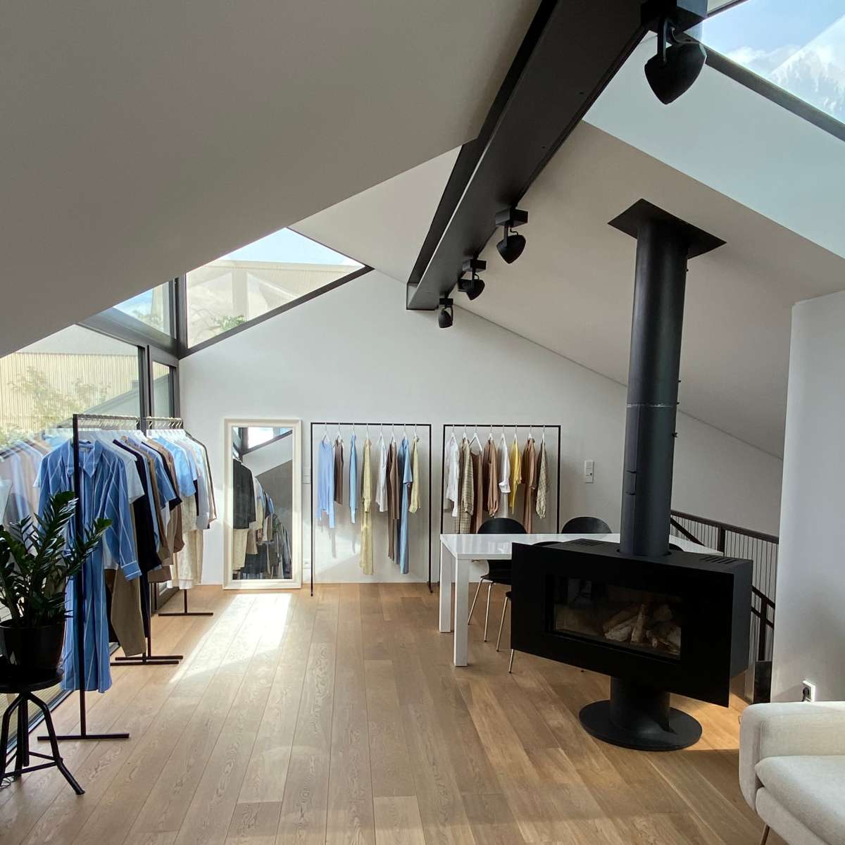 A modern clothing store with a range of garments displayed on racks, a mirror, and a black fireplace in a spacious, light-filled interior.