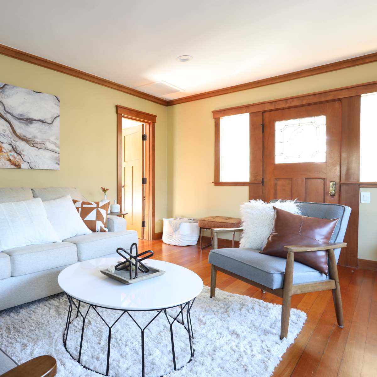 A modern living room features a light-colored sofa, a round coffee table, and wooden accents with a large abstract painting on the wall.