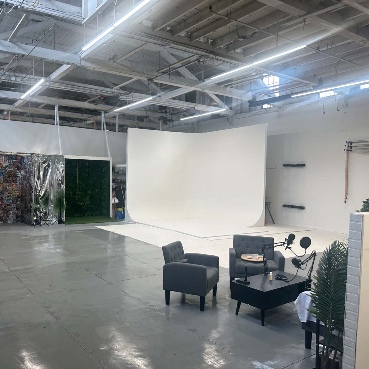An empty photography studio with a white backdrop, various props, and two gray chairs arranged around a small table.