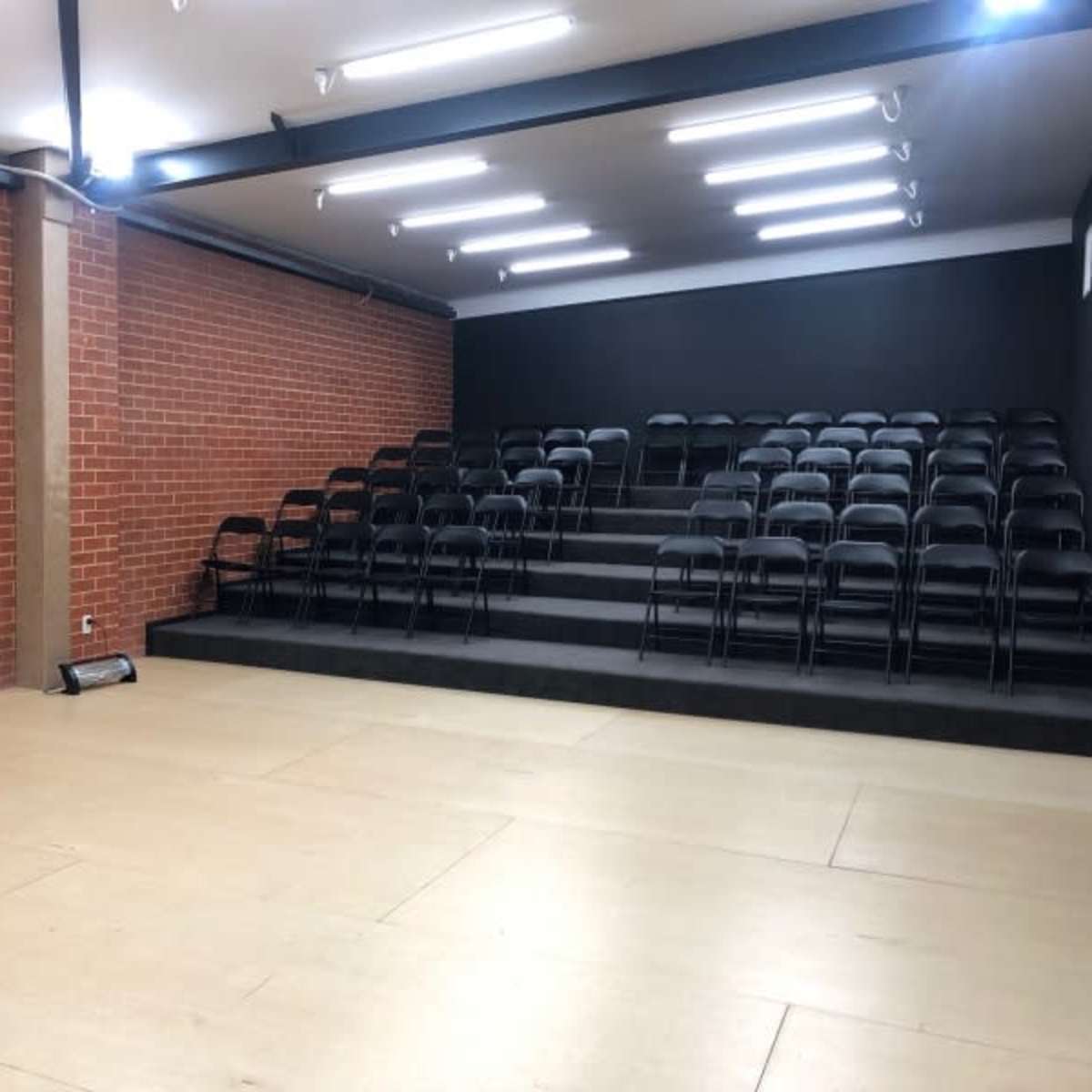 A rectangular room with a brick wall and tiered seating made of black chairs facing a blank wall.