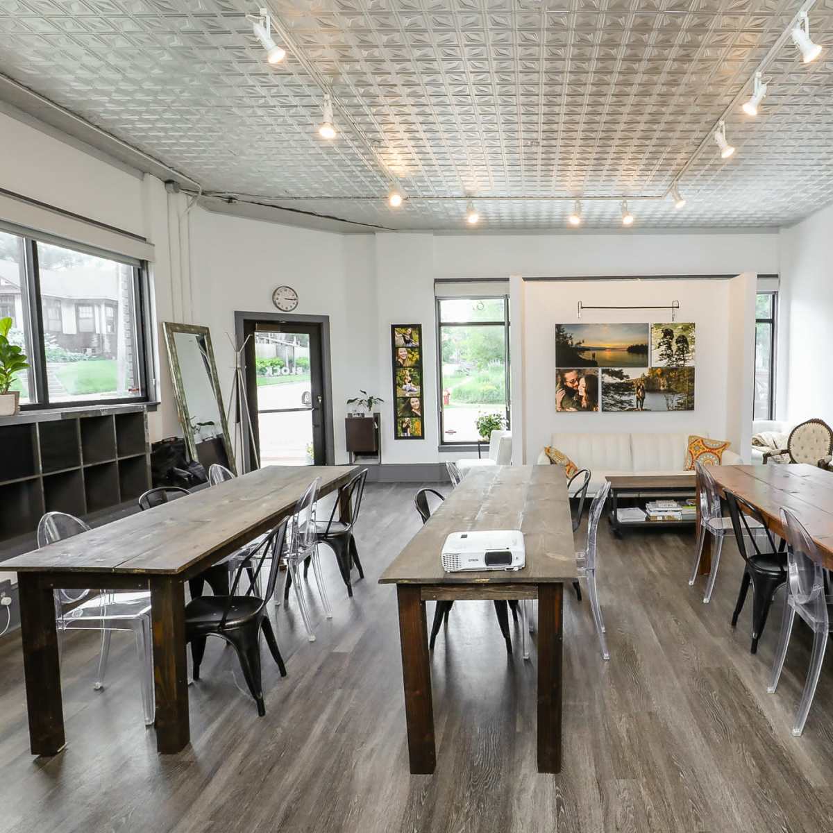 A spacious room with two wooden tables, clear chairs, and various framed photographs on the walls.