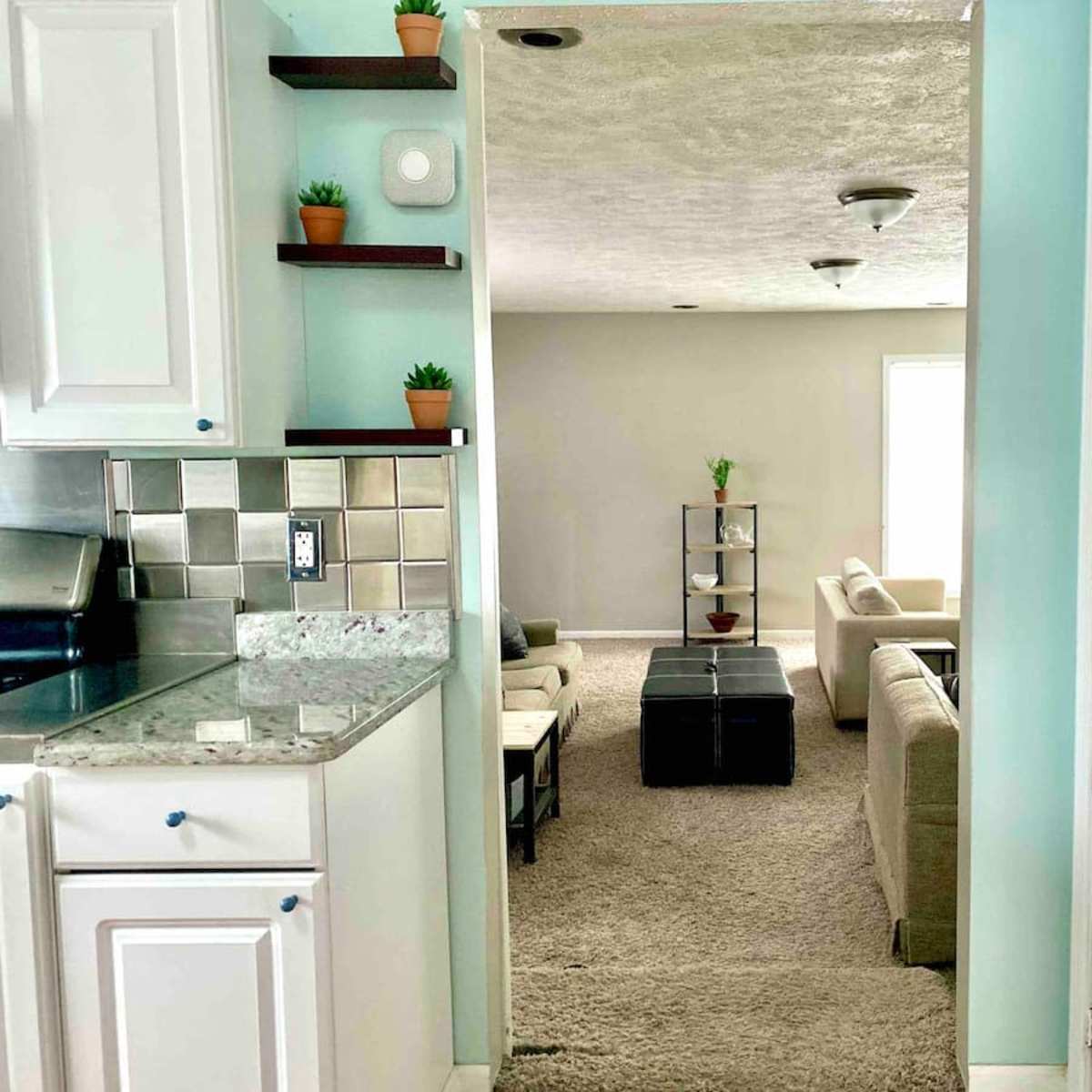 A view from a kitchen into a living room with beige furniture and a coffee table, separated by a doorway.