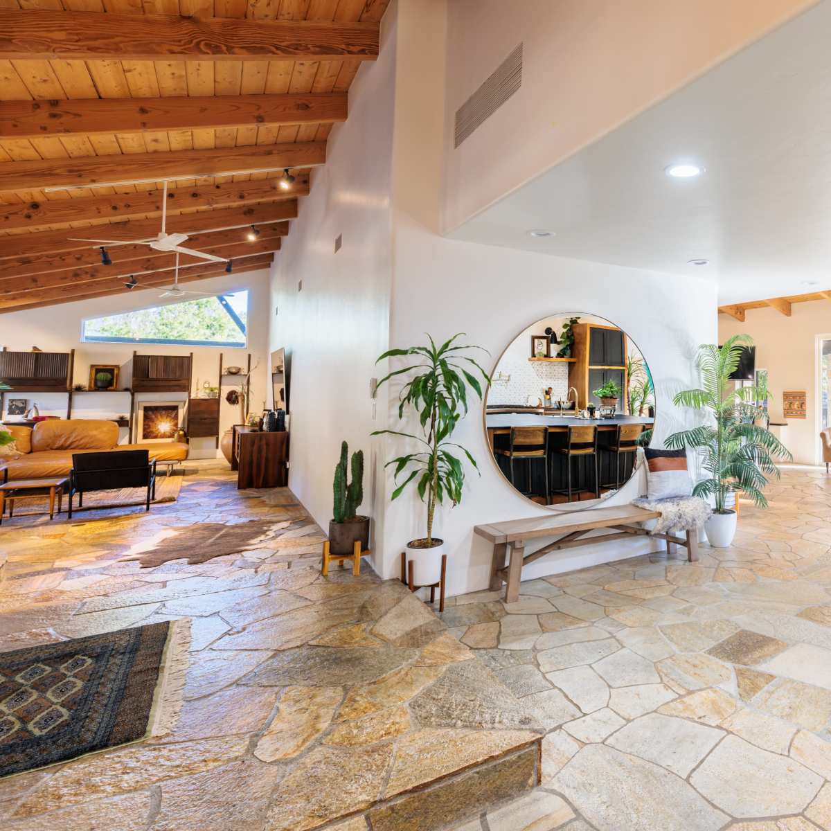 An open-concept living space featuring natural stone flooring, a circular mirror, a spacious kitchen island, and large windows allowing ample light.
